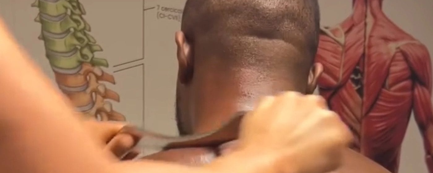 A therapist applying deep pressure to a client's neck and shoulder against anatomy charts