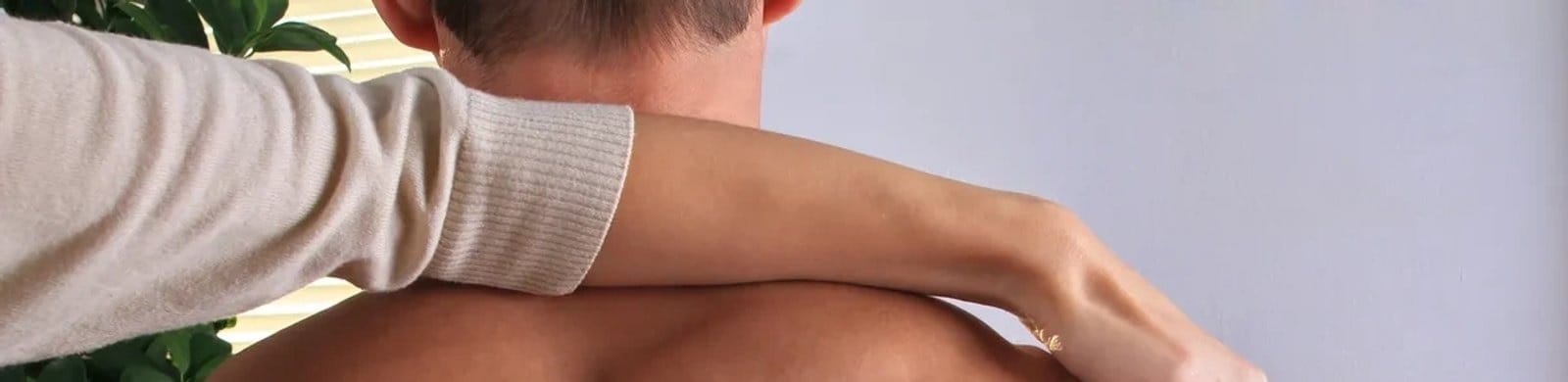 A therapist's forearm resting across a client's shoulder during a session